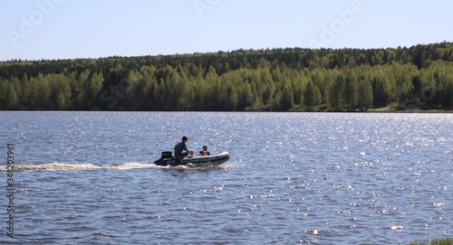 sparkling waves of a river or lake along which a rubber boat with a motor with two resting people rushes against the background of a forest on the far shore of a reservoir