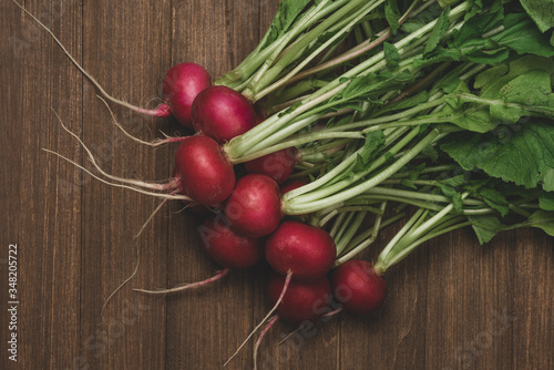 Fresh organic red radishes with green leaves on rustic wooden background. Top view with copy space. Healthy nutrition concept.