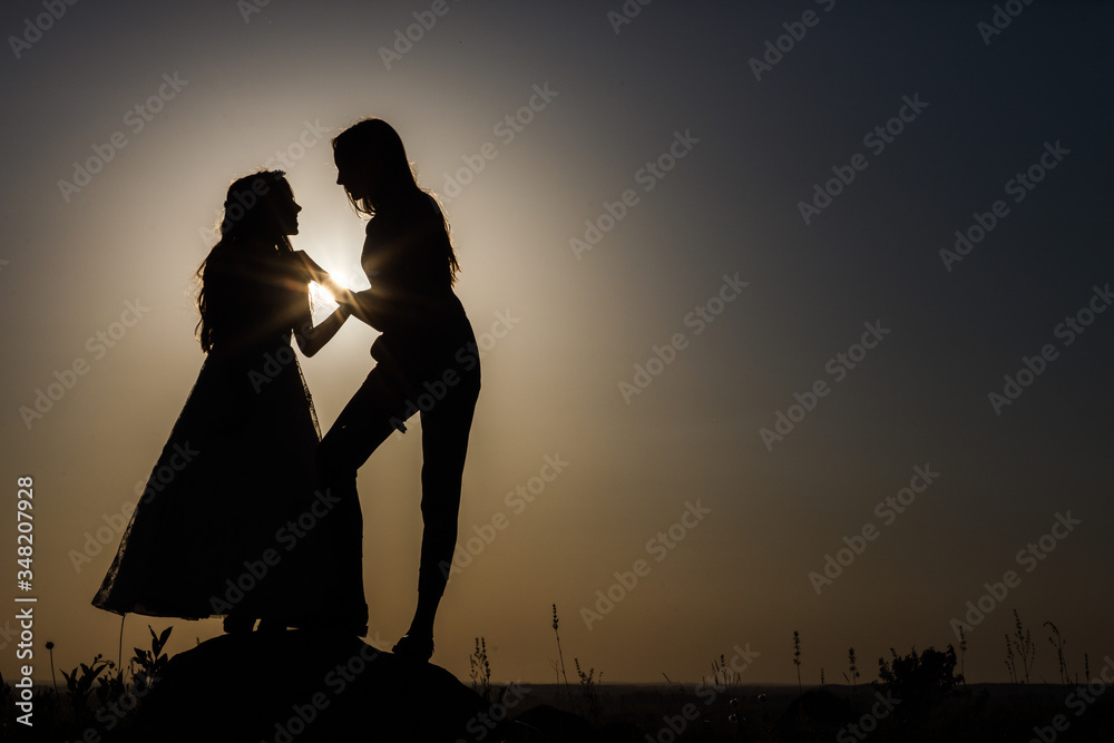Two sisters are standing next to each other. Silhouettes.