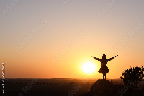 Silhouette of a girl standing on a rock and spreads her arms.