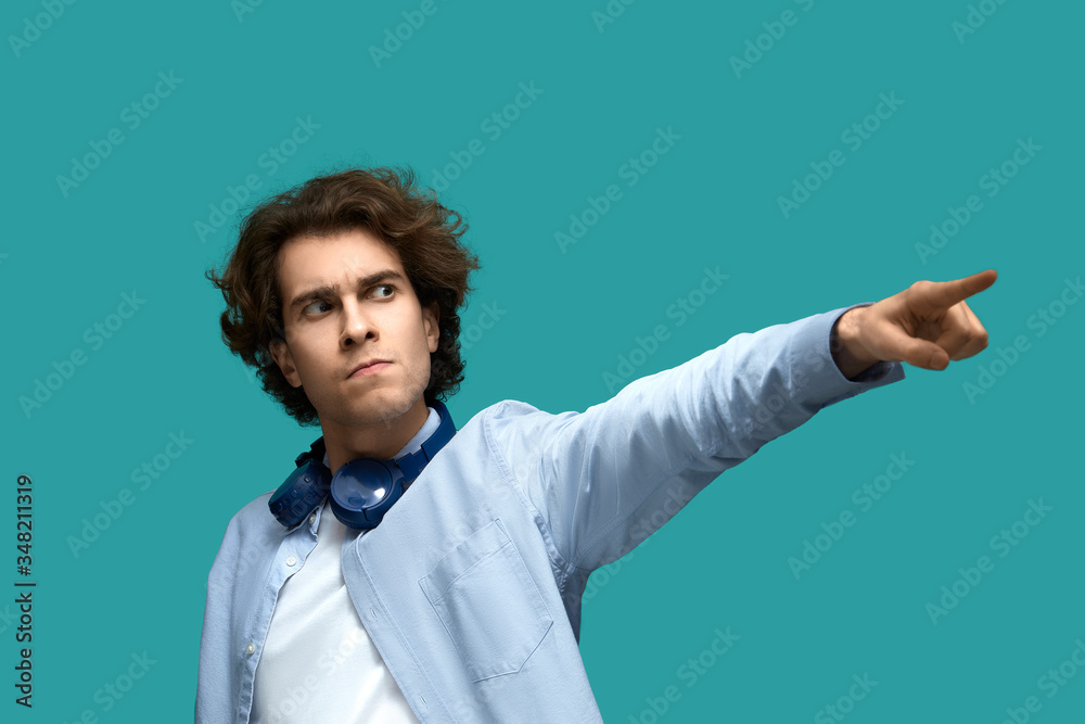 go there! Portrait of serious young beautiful man wearing white t-shirt and blue shirt in headphones point to something or somebody with a call by his forefinger go there! Portrait of serious young beautiful man wearing white t-shirt and blue shirt in headphones point to something or somebody with a call by his forefinger