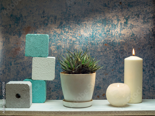 Room decoration with succulent plant and candle on white shelf against old blue wall.