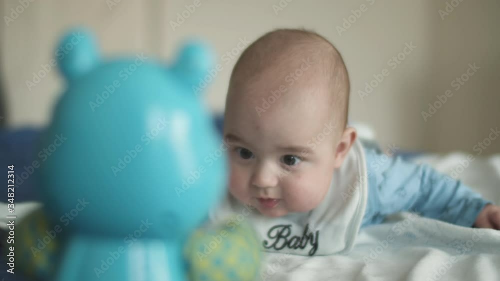 Cute little newborn baby boy enjoying while playing with his toys, child lying on the bed in a room at home. Close up shot. Cute little newborn baby boy enjoying while playing with his toys, child lying on the bed in a room at home. Close up shot.