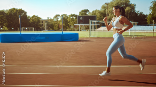 Beautiful Fitness Girl in Light Blue Athletic Top and Leggings Jogging in the Stadium. She is Running on a Warm Summer Afternoon. Athlete Doing Her Routine Sports Practice on a Track.