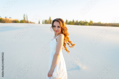 Attractive girl in a white dress walks on the sand in a white desert
