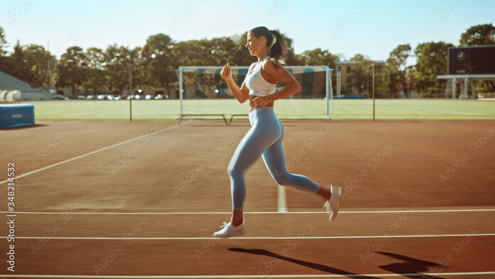 Beautiful Fitness Woman in Light Blue Athletic Top and Leggings Jogging in the Stadium. She is Running Fast on a Warm Summer Afternoon. Athlete Doing Her Routine Sports Practice.