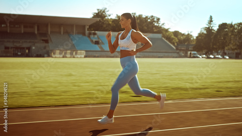 Beautiful Fitness Girl in Light Blue Athletic Top and Leggings Jogging in the Stadium. She is Running Fast on a Warm Summer Afternoon. Athlete Doing Her Routine Sports Practice.