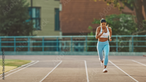 Beautiful Fitness Woman in Light Blue Athletic Top and Leggings is Starting a Sprint Run in an Outdoor Stadium. She is Running on a Warm Summer Day. Athlete Doing Her Sports Practice.