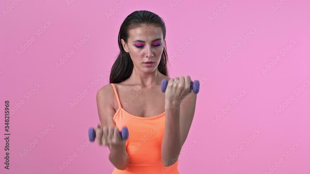 Young amazing fitness woman isolated over pink wall background make exercises with dumbbells Young amazing fitness woman isolated over pink wall background make exercises with dumbbells