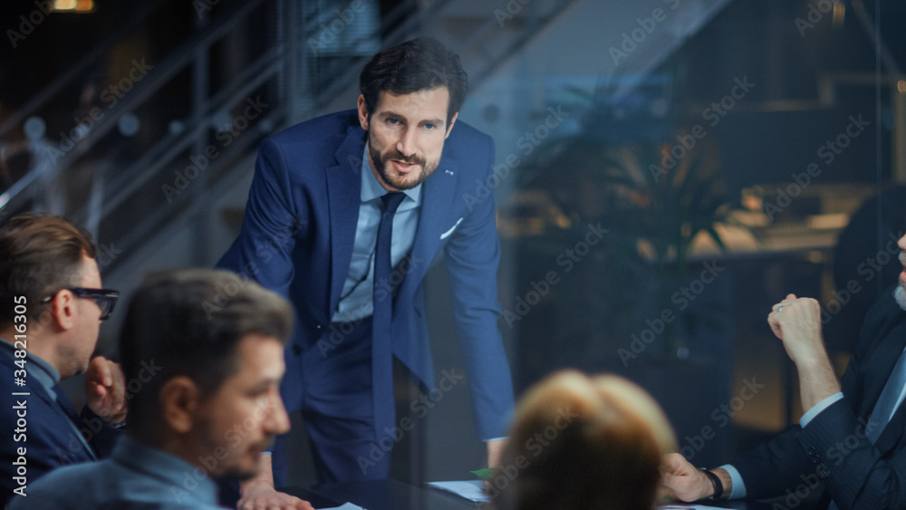Corporate Meeting Room: Confident and Handsom Executive Director Decisively Leans on a Conference Table and Delivers Report to a Board of Executives about Company’s Record Breaking Revenue Corporate Meeting Room: Confident and Handsom Executive Director Decisively Leans on a Conference Table and Delivers Report to a Board of Executives about Company’s Record Breaking Revenue