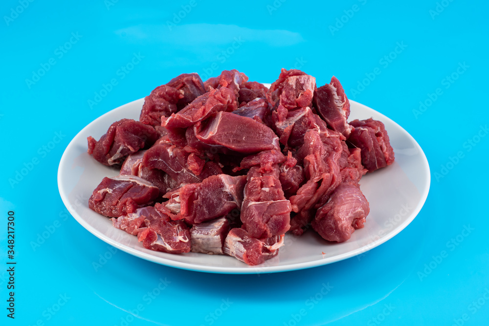 chopped small pieces of raw beef meat, tenderloin on a white plate on a blue background chopped small pieces of raw beef meat, tenderloin on a white plate on a blue background