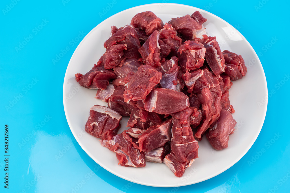 chopped small pieces of raw beef meat, tenderloin on a white plate on a blue background