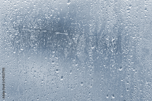 Raindrops, condensation on the glass window during heavy rain, water drops on blue glass