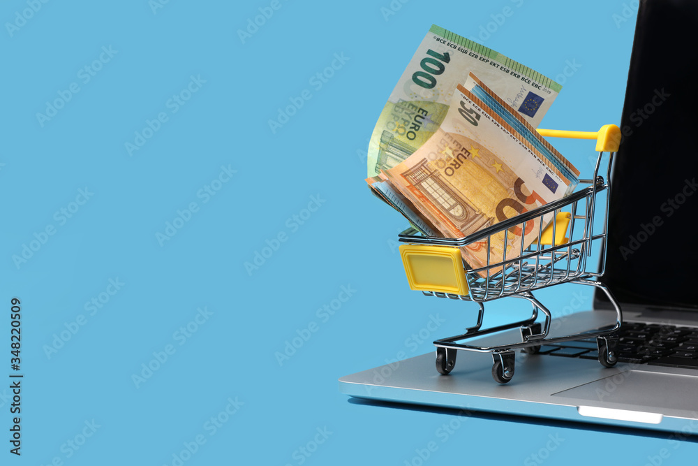 shopping cart with euro banknotes inside on laptop on blue background, shopping online concept.