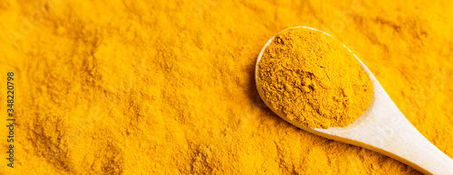 Close-up turmeric powder in wooden spoon at scattered curcuma banner