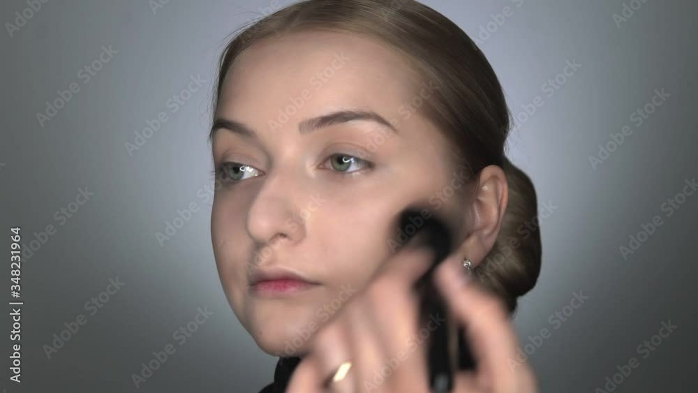 Make-up artist making professional make-up for young woman in beauty studio. Make up Artist applies powder with a big brush Make-up artist making professional make-up for young woman in beauty studio. Make up Artist applies powder with a big brush
