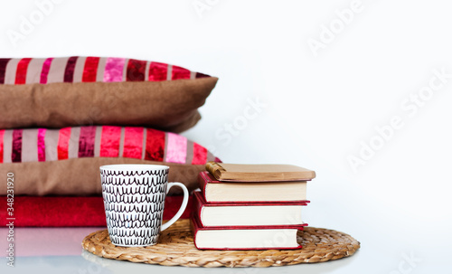 Cozy home interior decor: cup of coffee, stack of books, pillows and plaid on a white table. Distance home education. Quarantine concept of stay home.