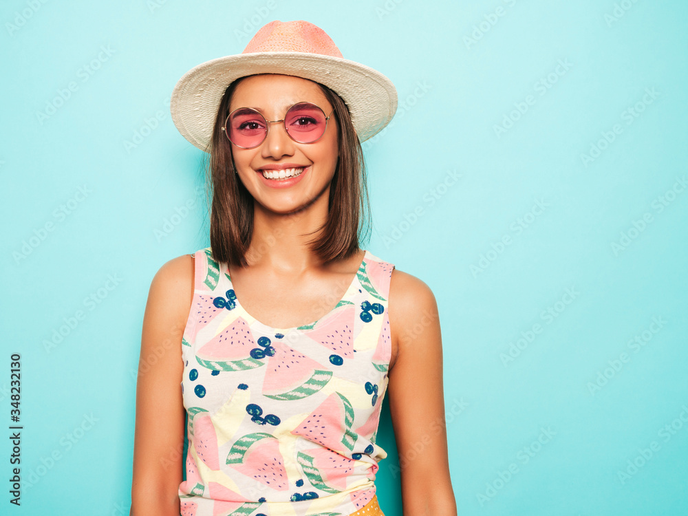 Young beautiful woman looking at camera in hat.Trendy girl in casual summer white T-shirt and yellow skirt in round sunglasses. Positive female shows facial emotions. Funny model isolated on blue Young beautiful woman looking at camera in hat.Trendy girl in casual summer white T-shirt and yellow skirt in round sunglasses. Positive female shows facial emotions. Funny model isolated on blue