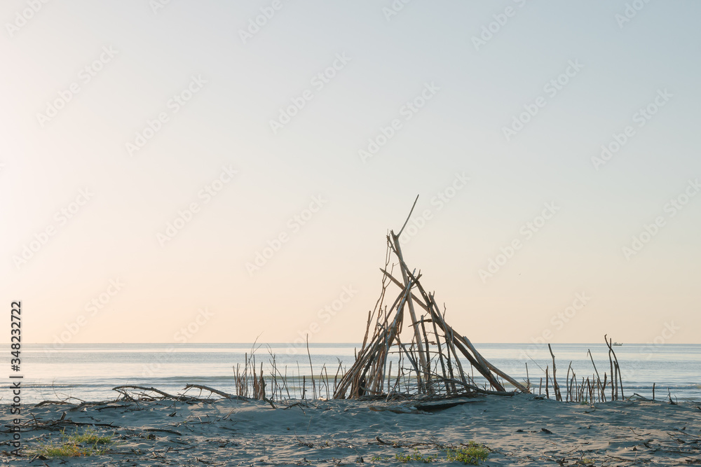 Seaside landscape in evening. Hut of branches on a beach. Relax in evening on the beach. Sunset at sea. Calm and sort seascape. Shelter of branches on the sand on the sea coast. Dry tree 
