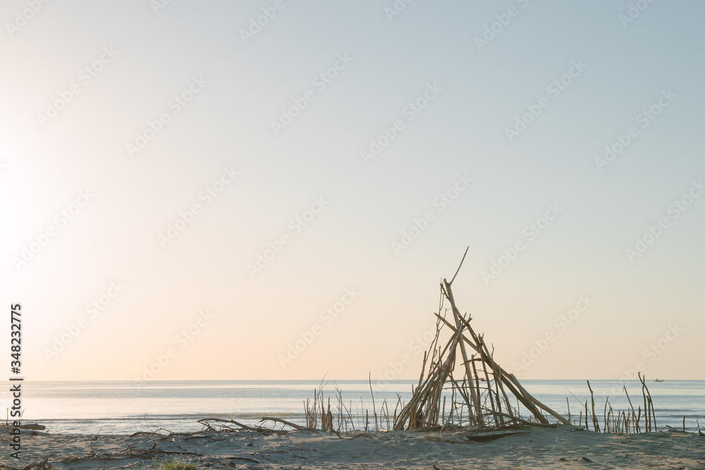 Seaside landscape in evening. Hut of branches on a beach. Relax in evening on the beach. Sunset at sea. Calm and sort seascape. Shelter of branches on the sand on the sea coast. 