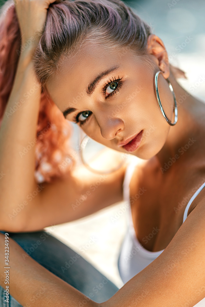 Capture her look. Close up portrait of a beautiful young caucasian woman with pink hair looking at camera while relaxing on a sunny day. Vertical shot