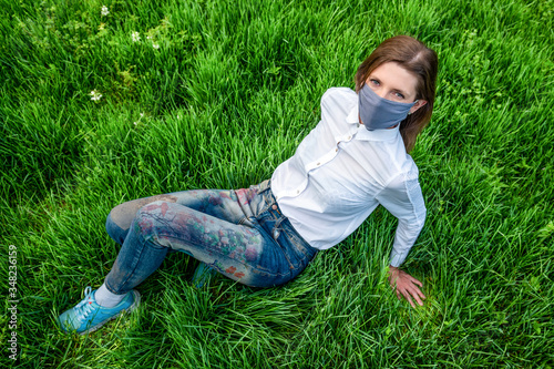 Medical mask, protection against coronavirus and other viruses. Woman sitting on grass and looking up at camera