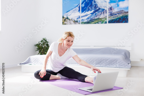 Beautiful young woman training online at home on laptop computer, copy space. Full length portrait. Yoga, pilates, working out exercising