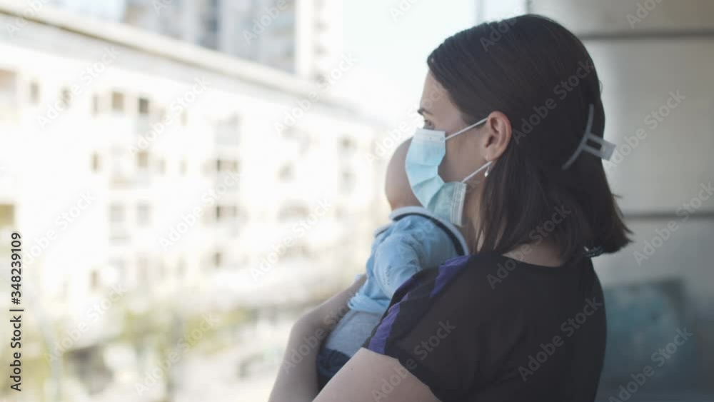 Mother wearing a protective mask on the face while taking care of a newborn baby boy during COVID-19 pandemic, quarantine outdoor life, free time.