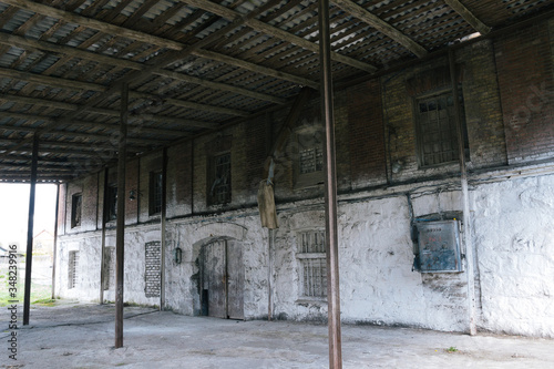 Old abandoned brick mill. White wall in old mill with wood roof. Stock for grains. Historical destroyed building in belarusian village. Ancient traditional two-storied mill with clogged window, door.