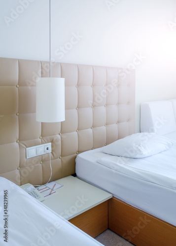 Sunny room in a hotel in light colors with two beds, bedside table and a lamp