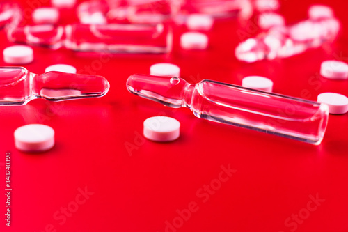 Ampoules for injections and white pills on a red background. Medical background. Copy space.