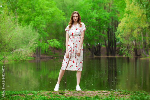 Portrait of a young beautiful woman in white dress posing by the lake