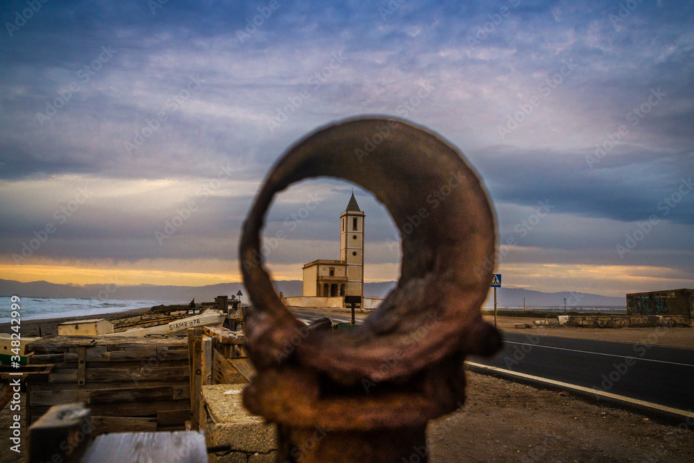Fototapeta premium The iconic church of San Miguel seen through rusty fishing gear at sunset, Las Salinas, Cabo de Gata-Níjar Natural Park, Almería, Andalusia, Spain