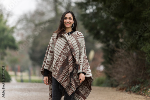 Murais de parede Young Indian woman wearing poncho smiling toothy smile at camera outdoors