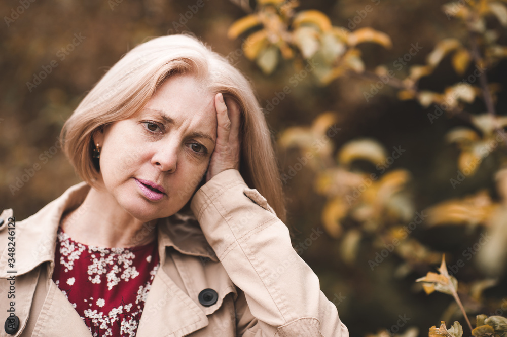 Sad adult woman 55-60 year old having headache holding head over nature  background outdoors closeup. Mature. Healthy lifestyle. Wellness.  фотография Stock | Adobe Stock