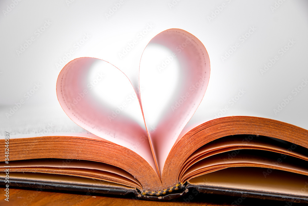 Old book and heart-shaped pages. White background. Wooden Table. Closeup Old book and heart-shaped pages. White background. Wooden Table. Closeup