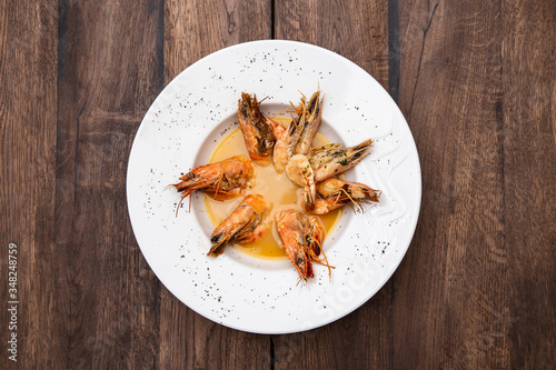 Tiger prawns with garlic and pepper, boiled in broth in a white plate on a wooden table. photo