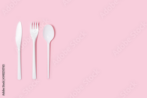 Cuchillo, tenedor y cuchara de plástico blanco desechable sobre fondo rosa liso y aislado. Vista superior. Copy space