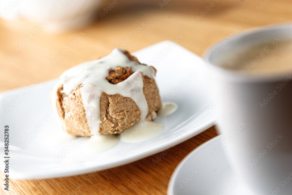 Cinnamon Bun with Icing and coffee cappucino ready to eat on a white plate with a white mug Cinnamon Bun with Icing and coffee cappucino ready to eat on a white plate with a white mug