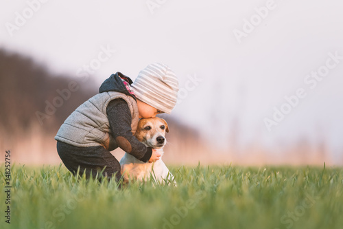 Photography Small kid in yellow jacket with jack russel terrier puppy embrace one another on