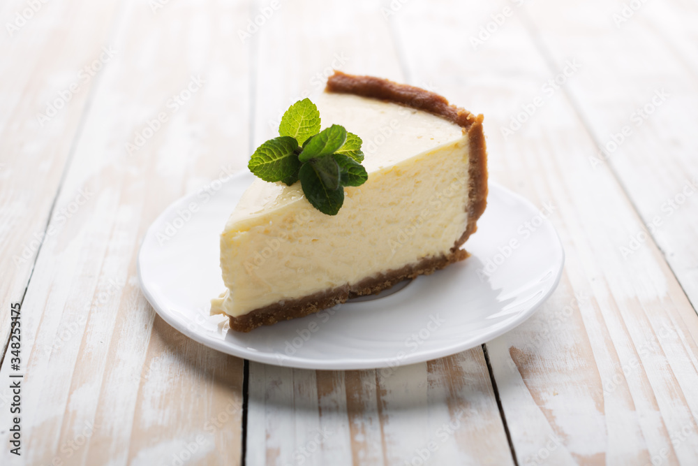Slice of classic New York cheesecake with a sprig of mint on a plate on a wooden table. The concept of bakery and sweet cakes desserts