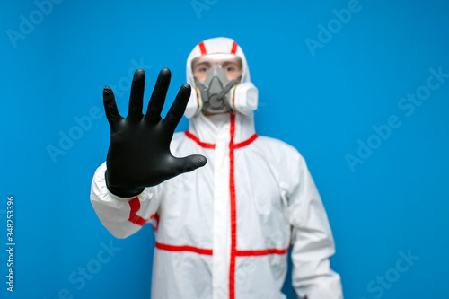 resistance to coronavirus. disinfection worker in protective equipment and respirator shows a stop sign, virologist on blue background