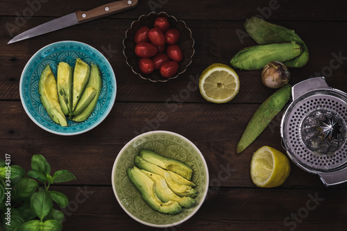 Two bowls with sliced avocado, tomatoes and lemon on a wooden table