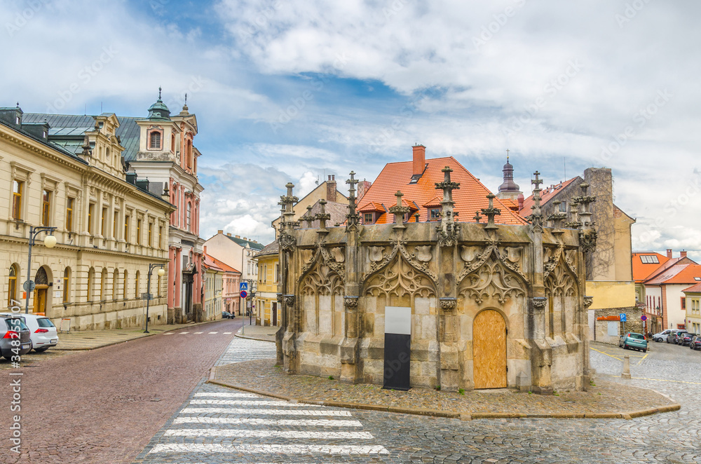 Stone Fountain in Kutna Hora historical Town Centre with cobblestone road, old style buildings, blue cloudy sky background, Central Bohemian Region, Czech Republic