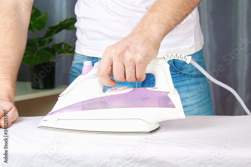 A man strokes linen with an electric iron on an ironing board. Household.