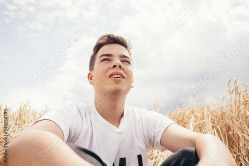 Portrait of pensive handsome teenage boy outdoors  sitting on wheat field  at summer day.
