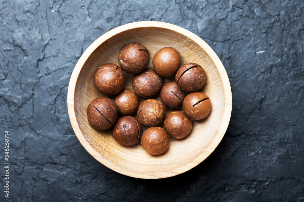 Obraz premium Dried organic Macadamia nuts in wooden bowl closeup. Studio macro shoot. Black concrete background