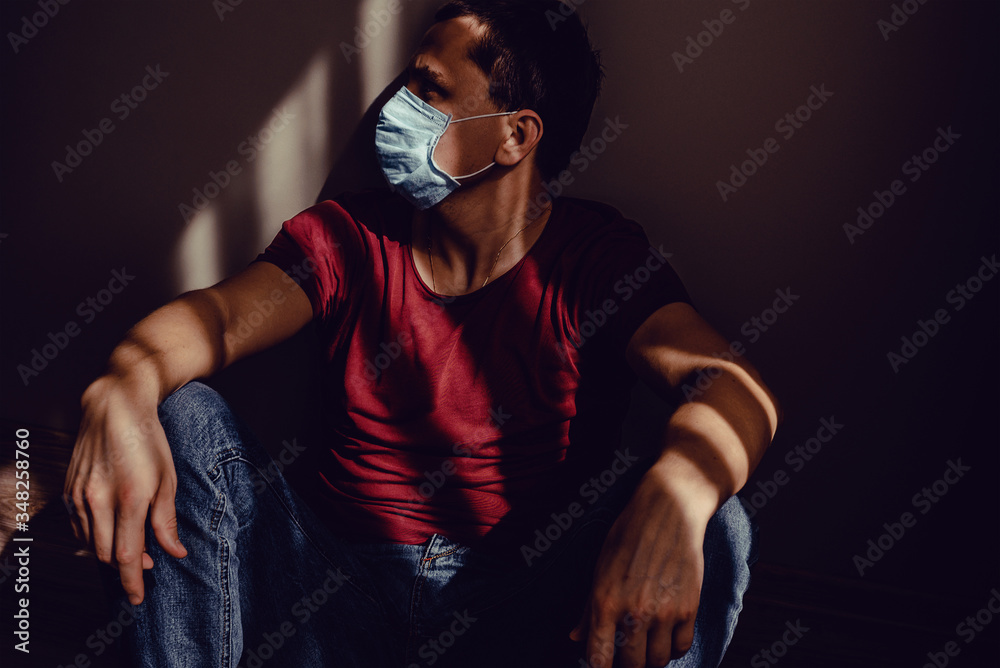 Sad thoughtful adult man sideview profile portrait in medical mask sit leaning wall with light and shadow pattern. Stay isolation at home. Quarantine concept. Pandemic Coronavirus. Social Distancing Sad thoughtful adult man sideview profile portrait in medical mask sit leaning wall with light and shadow pattern. Stay isolation at home. Quarantine concept. Pandemic Coronavirus. Social Distancing
