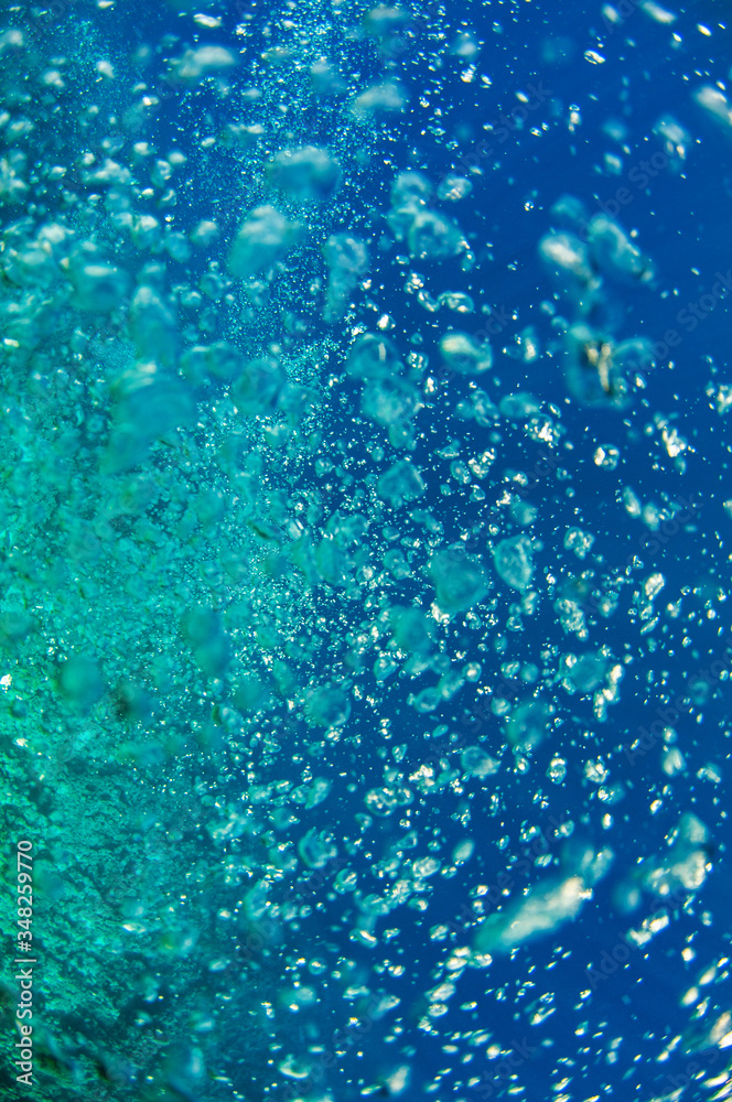 A close view at the coral reef sunlit. Air bubbles emitted by a diver who hidden under the deep dark ocean blue water column.Male in flippers examines the seabed.Floating fish looking for food.