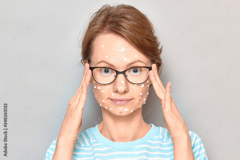 Portrait of positive girl with white drops of face cream on skin